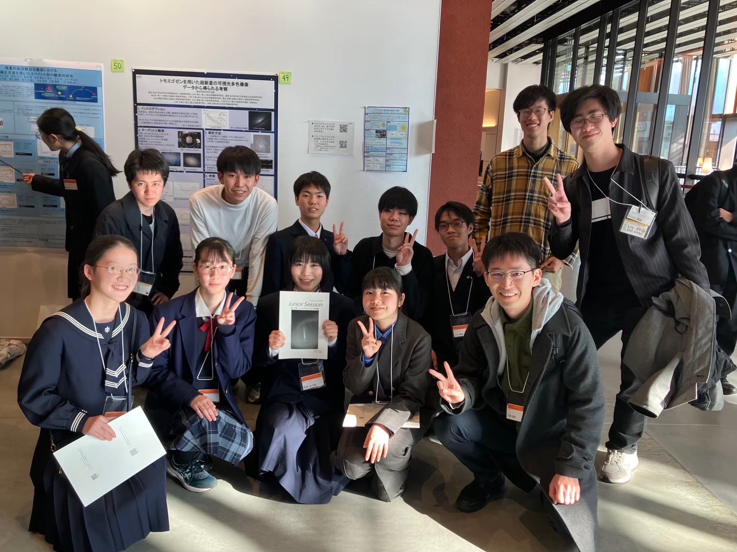 ポスター前で記念撮影をするB班の生徒と班長・TA。受講者と講師が2列になって写っており、笑顔がこぼれる。